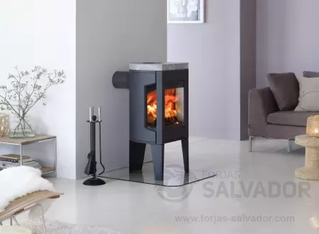 Estufa Jøtul F 163 instalada en un salón moderno con acabados de hierro fundido y diseño de tres patas.